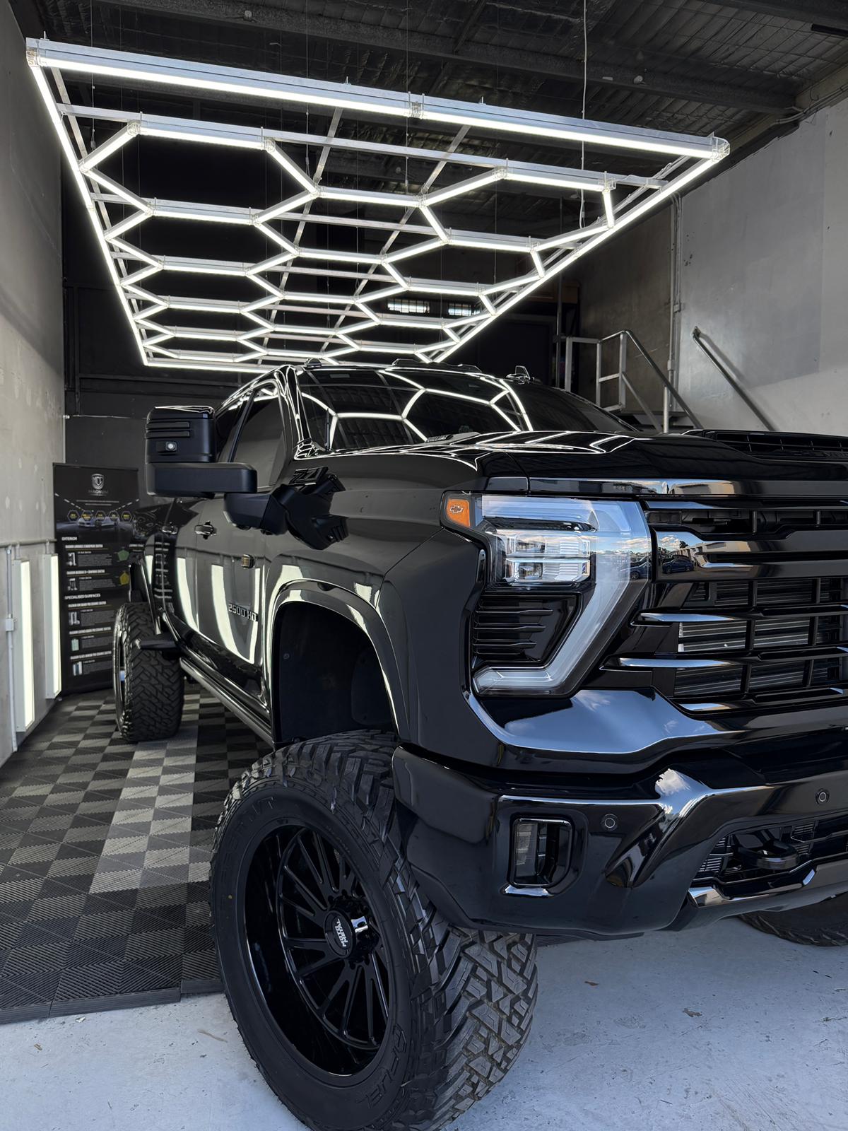 Black lifted Chevy Silverado HD2500 low-front angle in the A1 Auto Styling workshop, hexagonal LED ceiling reflected on the bonnet